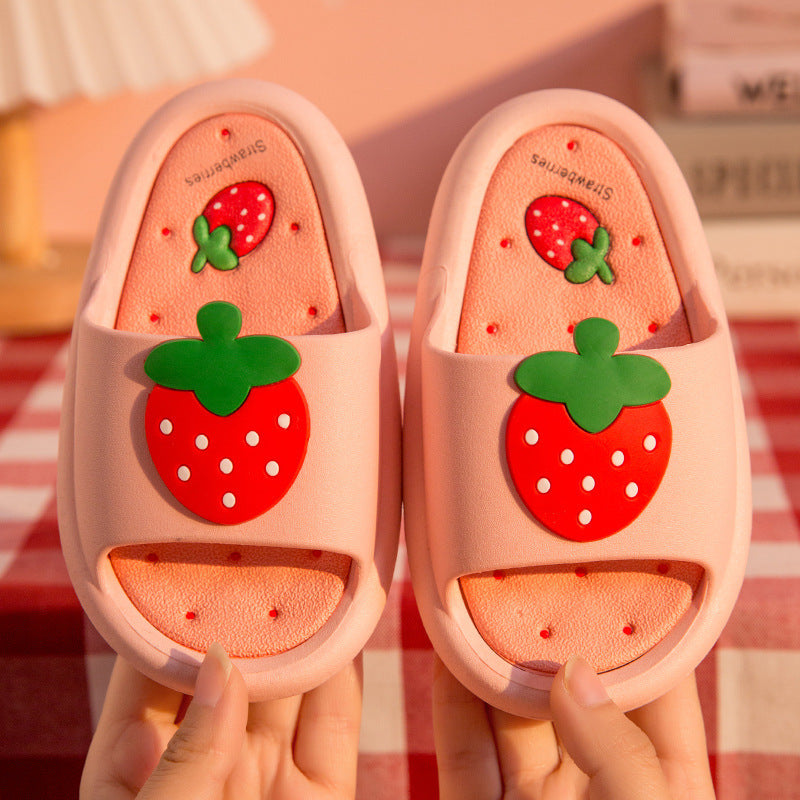 Pair of pink slippers with strawberry design held by a hand on a checkered background