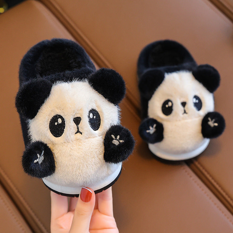 Pair of panda-shaped slippers held by a hand with red nail polish on a brown surface.