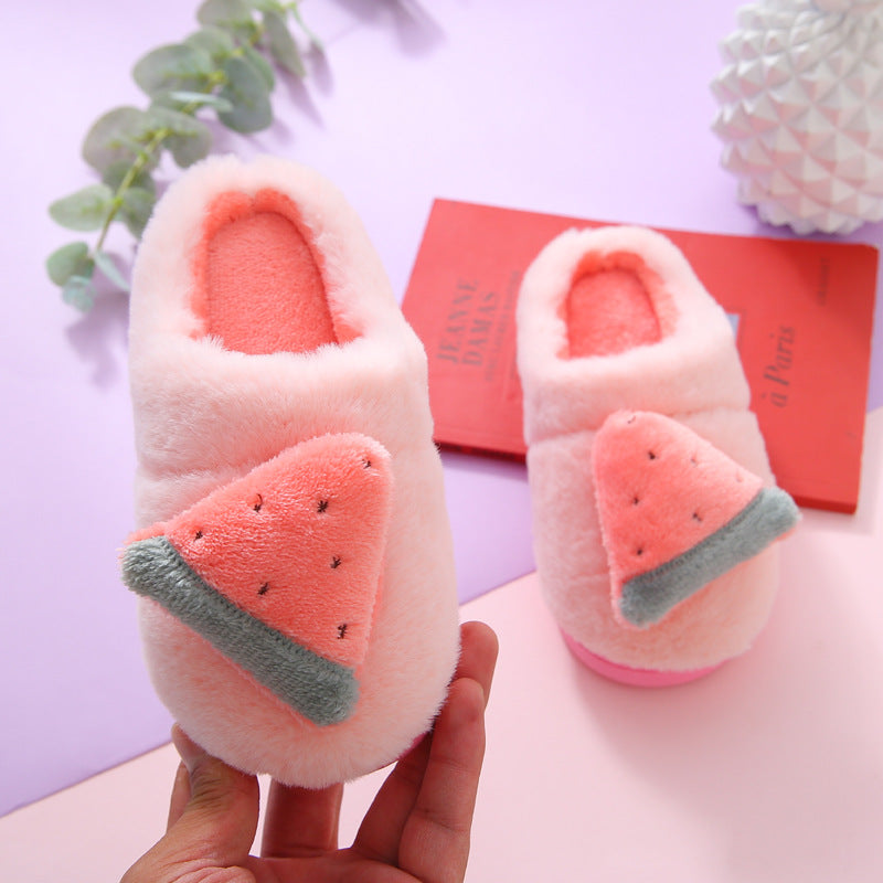 Pair of pink slippers with watermelon design held by a hand on a light purple background.