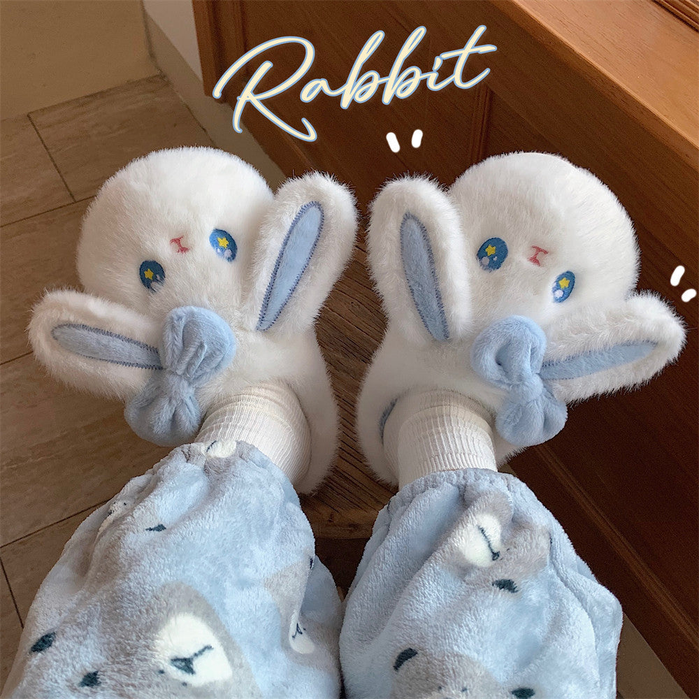 Pair of white bunny fuzzy slippers with blue accents held by a hand