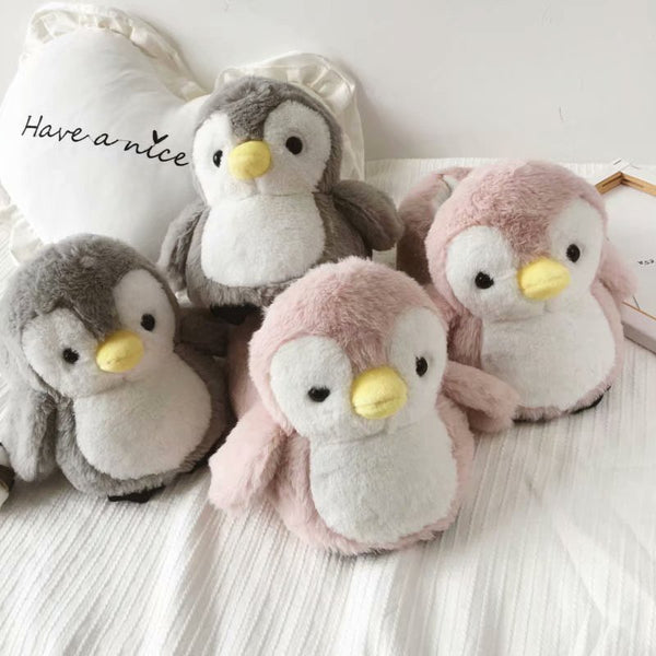 Four plush penguin slipper in gray and pink on a white surface with a soft focus background.