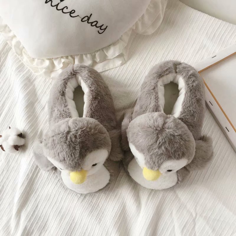 Pair of gray penguin slippers on a light surface with a white pillow in the background.