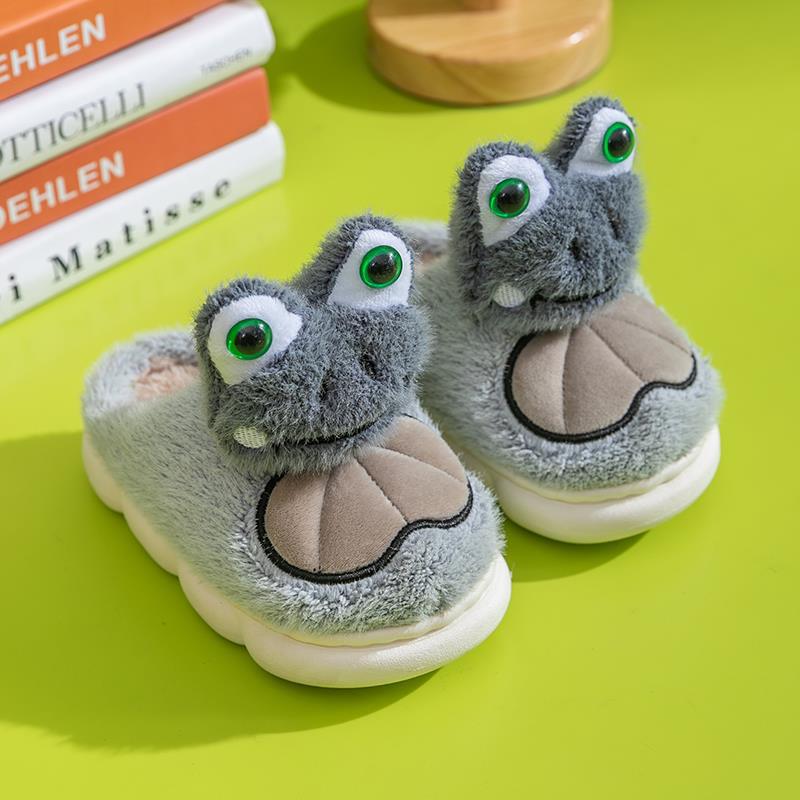 Pair of gray plush slippers with green eyes of frog on a green surface
