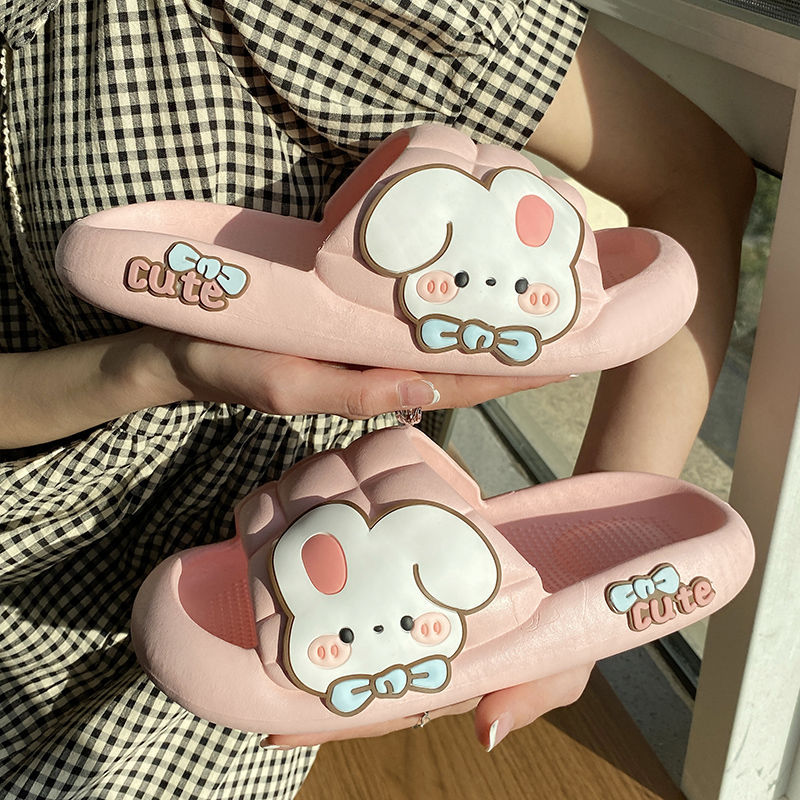 Cute pink slippers with cartoon rabbi design held by a person wearing a checkered shirt.