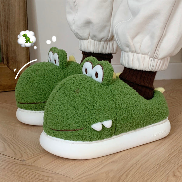 Green cartoonish Dinosaur slippers worn by a person on a wooden floor.