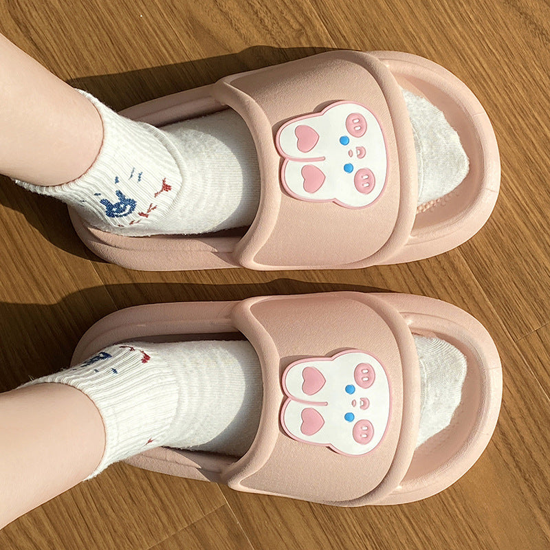Pink slippers with cartoon rabbit design worn by a child on a wooden floor.