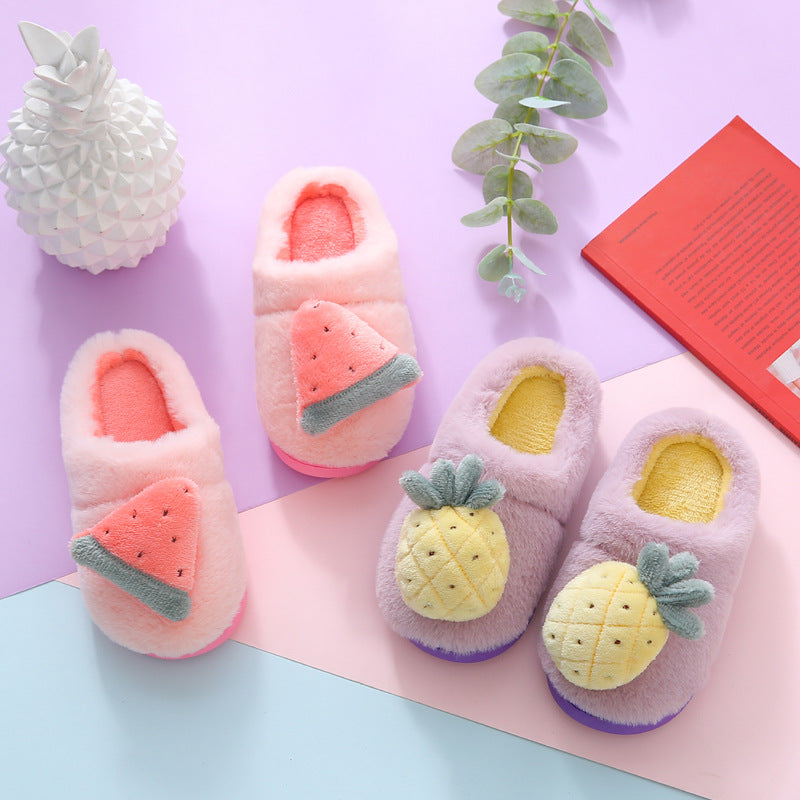Pair of pink slippers with watermelon design and a pair of purple slippers with pineapple design on a light purple background.
