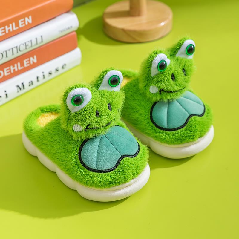 Green frog-themed children's slippers on a green surface with books in the background.