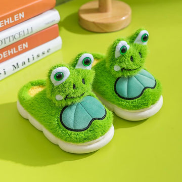 Green frog-themed children's slippers on a green surface with books in the background.