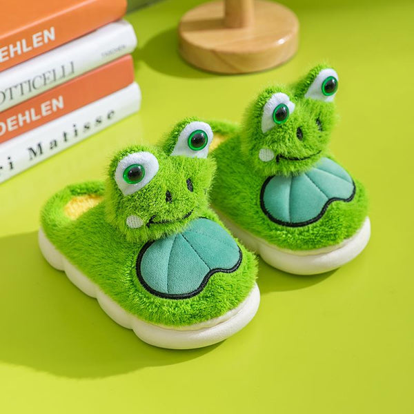 Green frog-themed children's slippers on a green surface with books in the background.