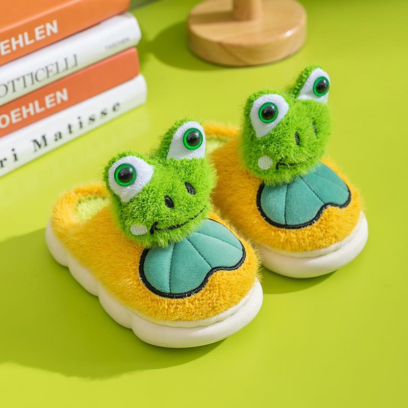 Green frog-themed children's shoes on a yellow surface with books in the background.
