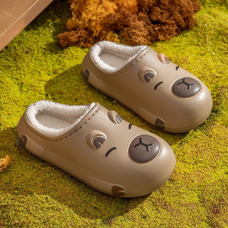 Pair of capybara beige slippers with facial expressions on a green surface