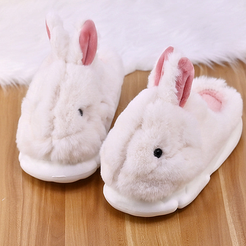 Pair of white bunny slippers with pink ears on a wooden floor.