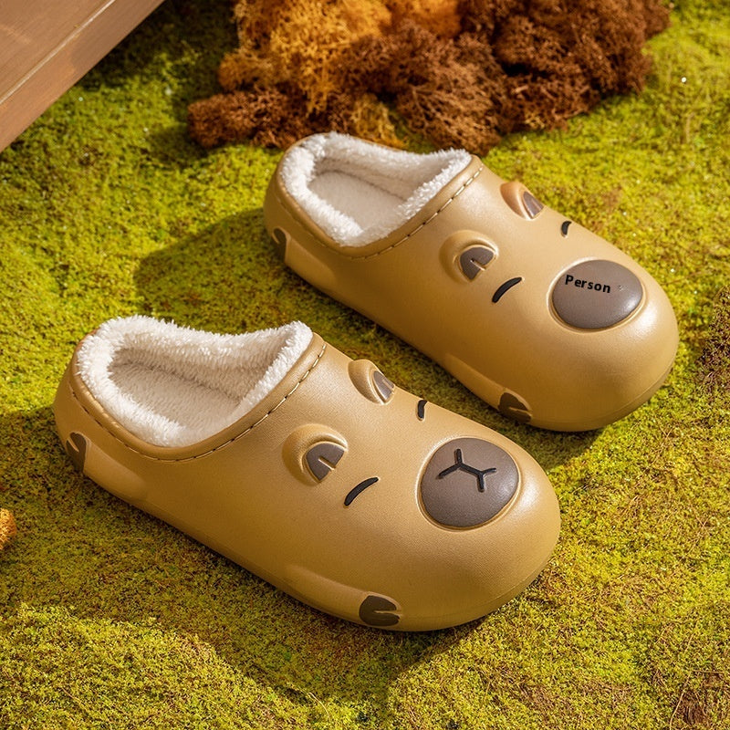 Pair of capybara beige slippers with facial expressions on a green surface