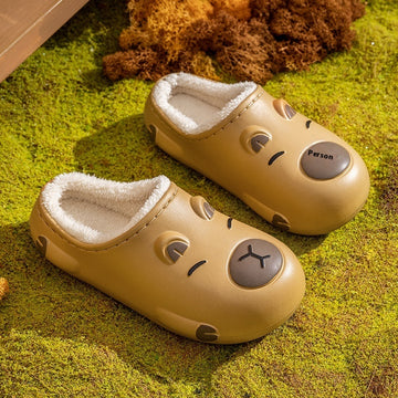 Pair of capybara beige slippers with facial expressions on a green surface