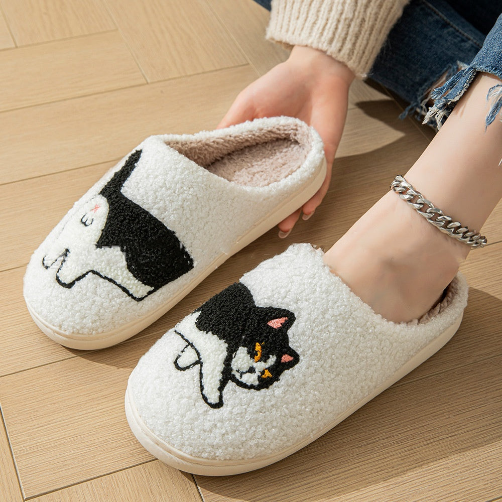 White slippers with black cat design held by a person on a wooden floor