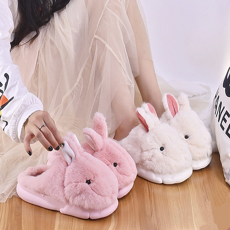 Pink and white bunny slippers on a wooden floor.