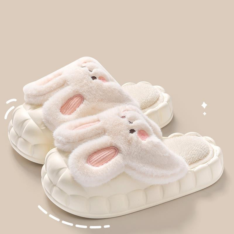 Pair of white bunny slippers with pink inner soles on a beige background