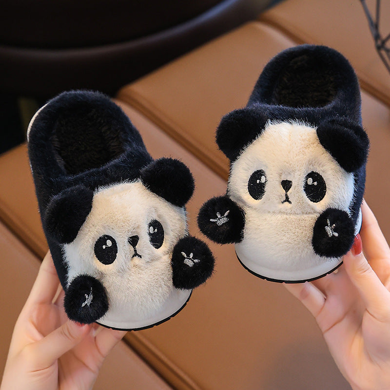 Pair of panda-themed slippers held by a person on a wooden floor.