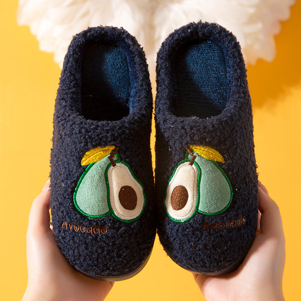 Pair of dark blue slippers with avocado design held against a yellow background