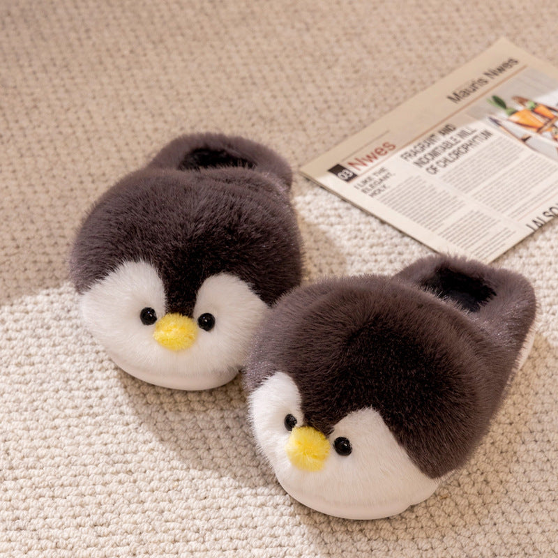 Pair of penguin-shaped slippers on a textured surface with a newspaper in the background.