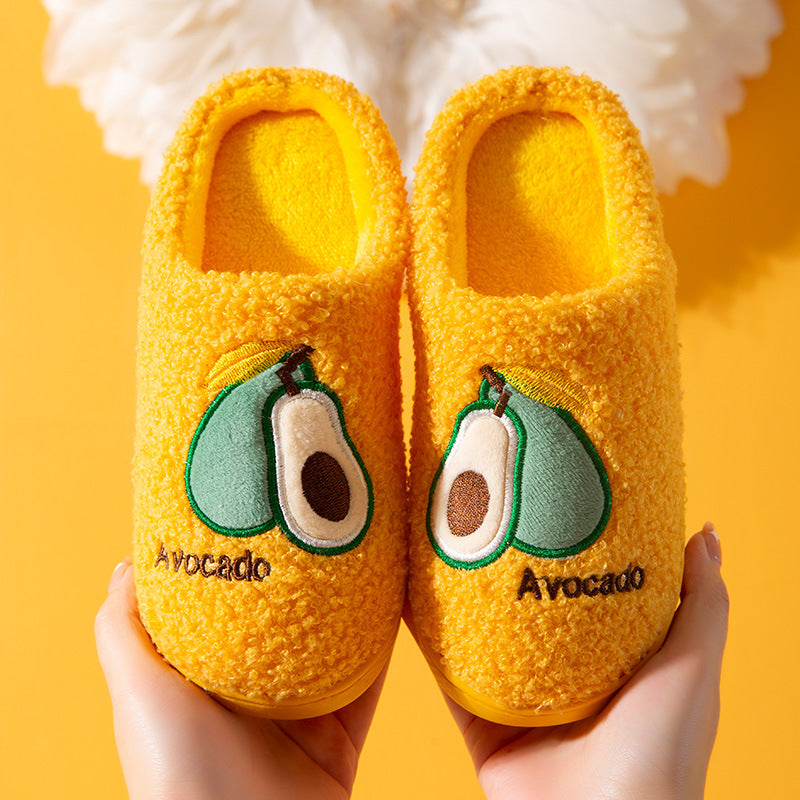 Yellow slippers with avocado design held against a yellow background