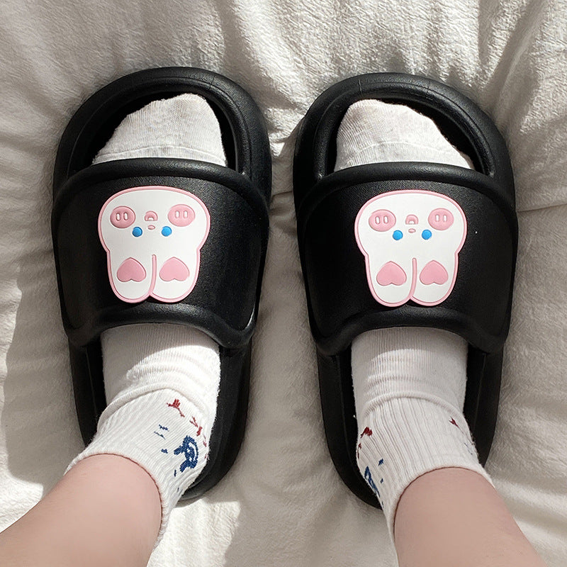 Black slippers with cartoon rabbit face design worn by a child on a white blanket