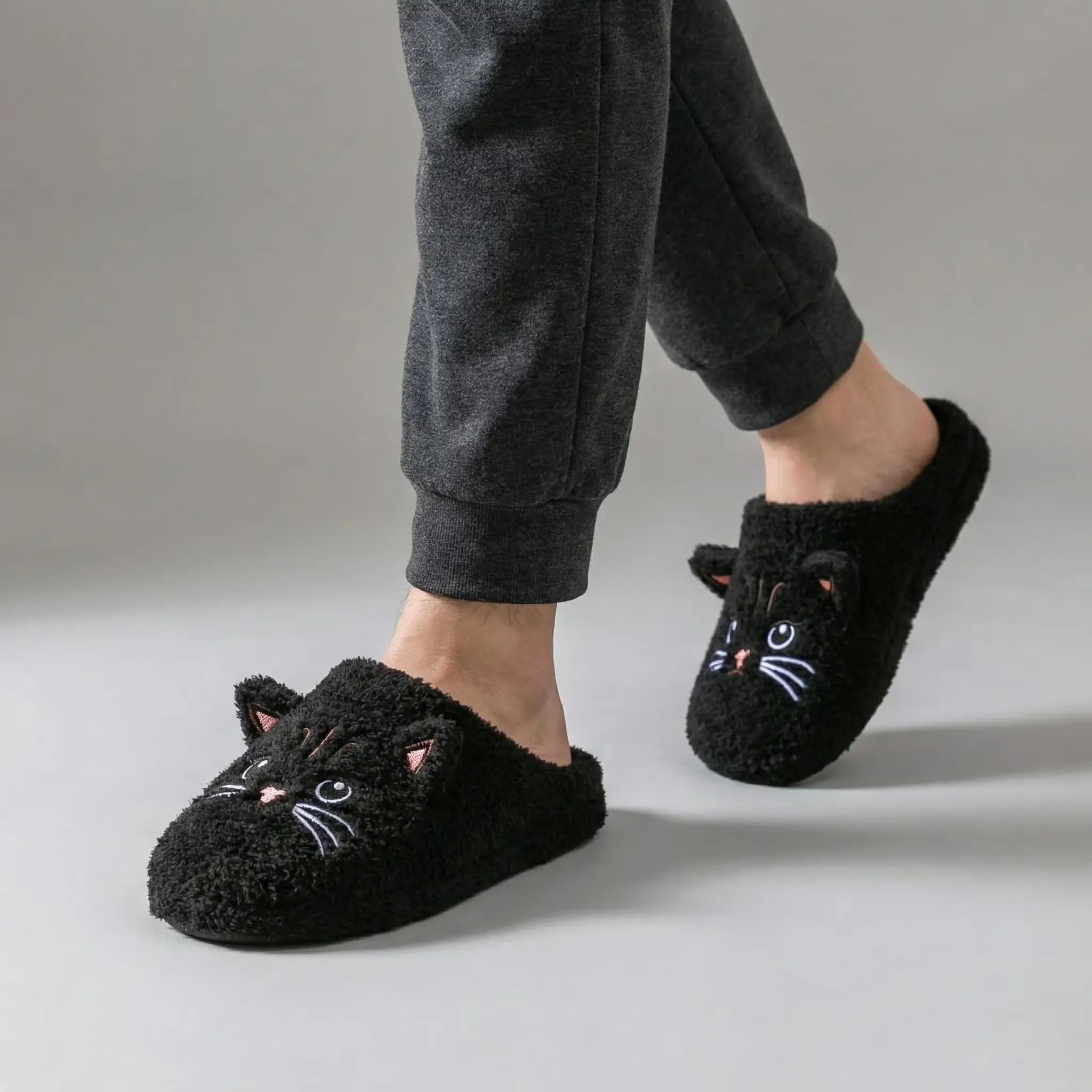 Black cat-themed slippers worn with gray pants on a neutral background