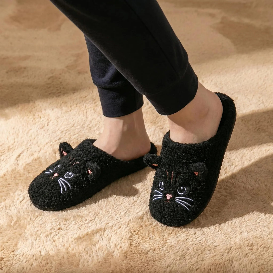 Black cat-shaped slippers worn on a beige carpet