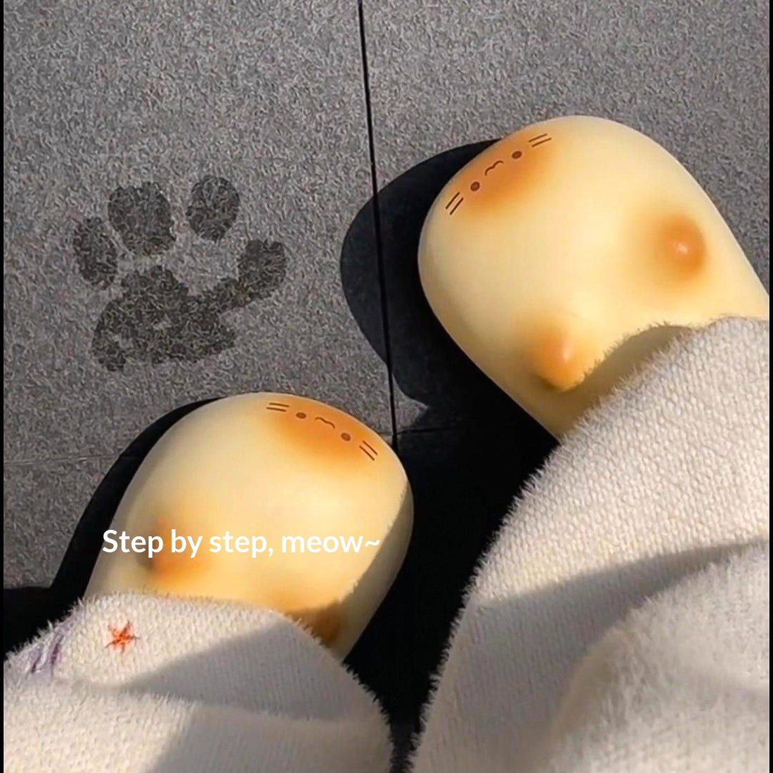 Feet wearing socks with a pattern of black paw prints on a gray surface with yellow leaves.