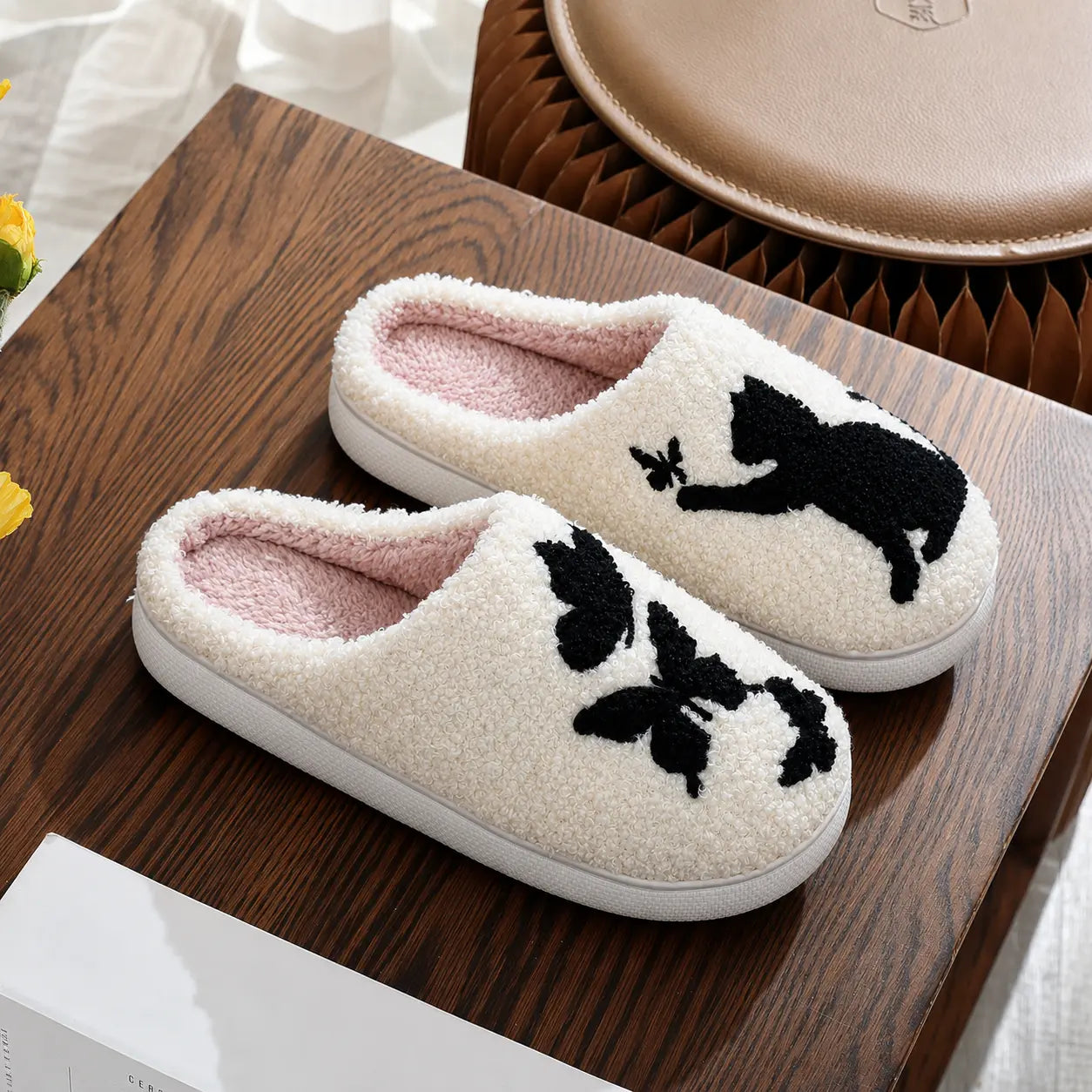 Pair of white slippers with black cat designs on a wooden surface.