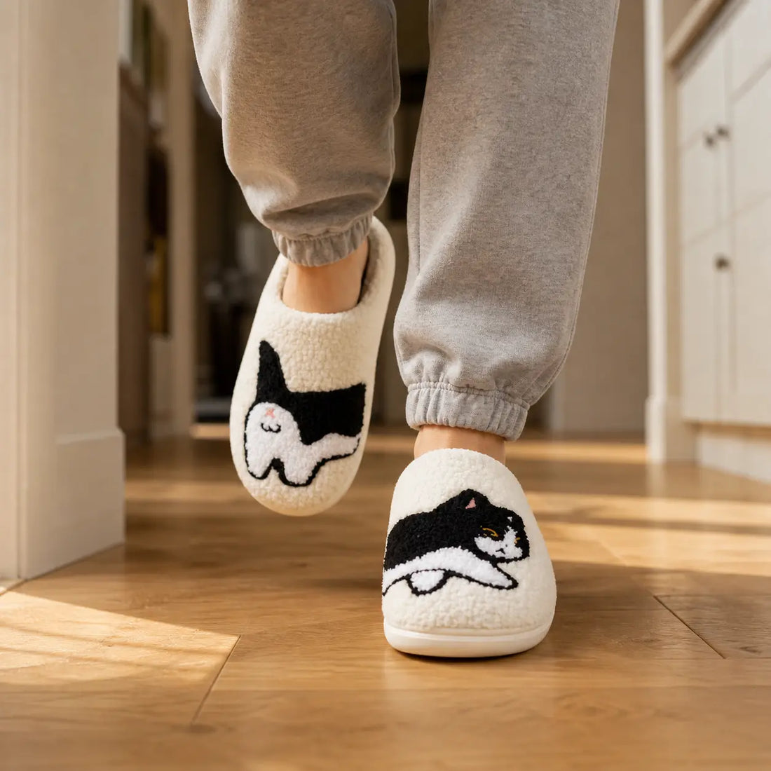 White slippers with black cat design held by a person on a wooden floor