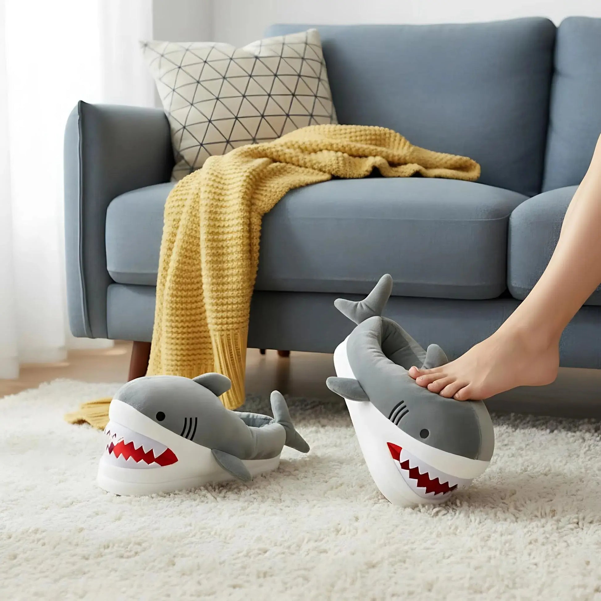 Shark-shaped slippers on a carpeted floor with a couch and yellow blanket in the background.