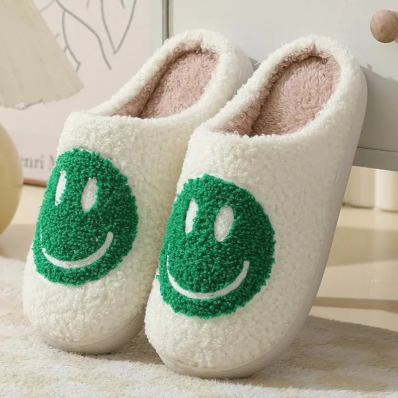 White slippers with green smiley face designs on a soft surface.
