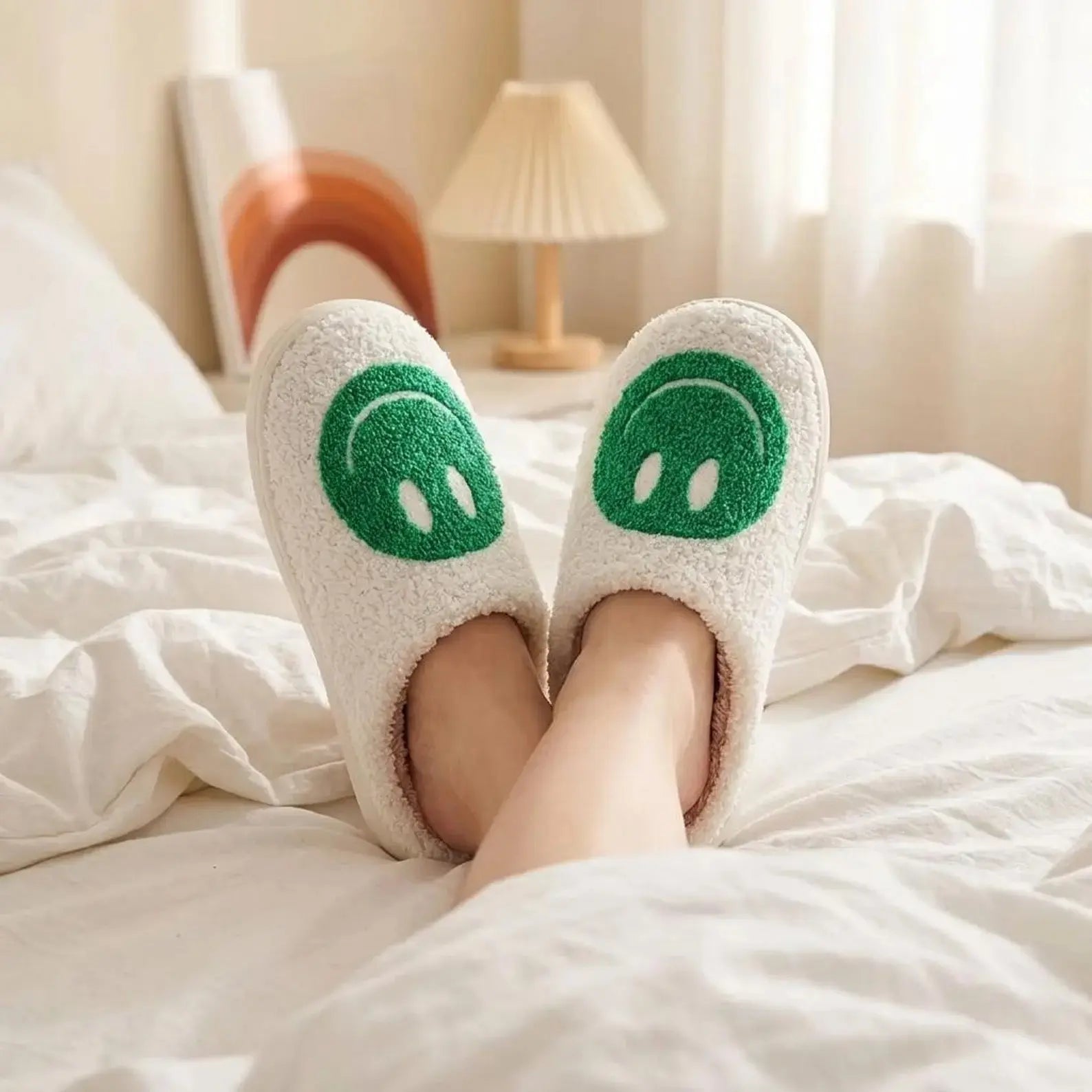 White slippers with green cartoon faces worn on a bed