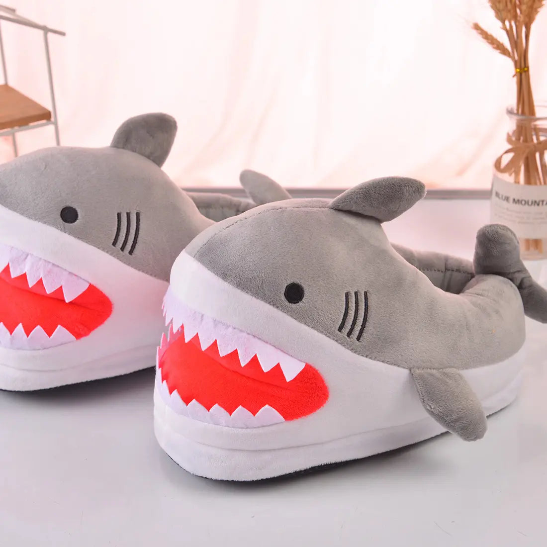 Shark-shaped slippers with red mouths on a light surface.