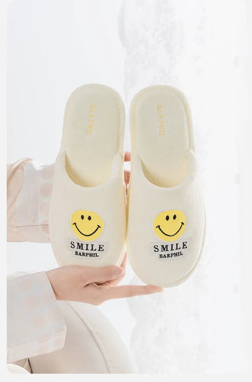 White slippers with smiley face design held by a person on a white background