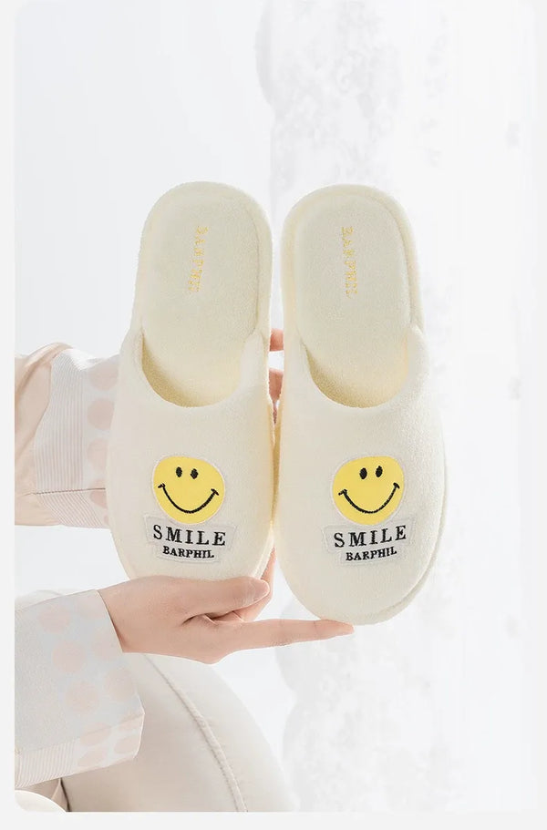 White slippers with smiley face design held by a person on a white background