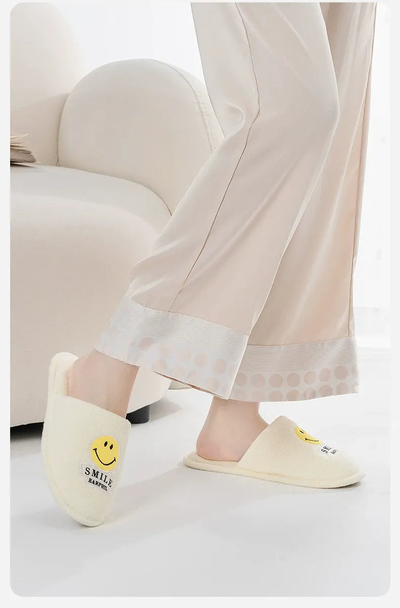 Person wearing light-colored slippers with smiley face design in a home setting.