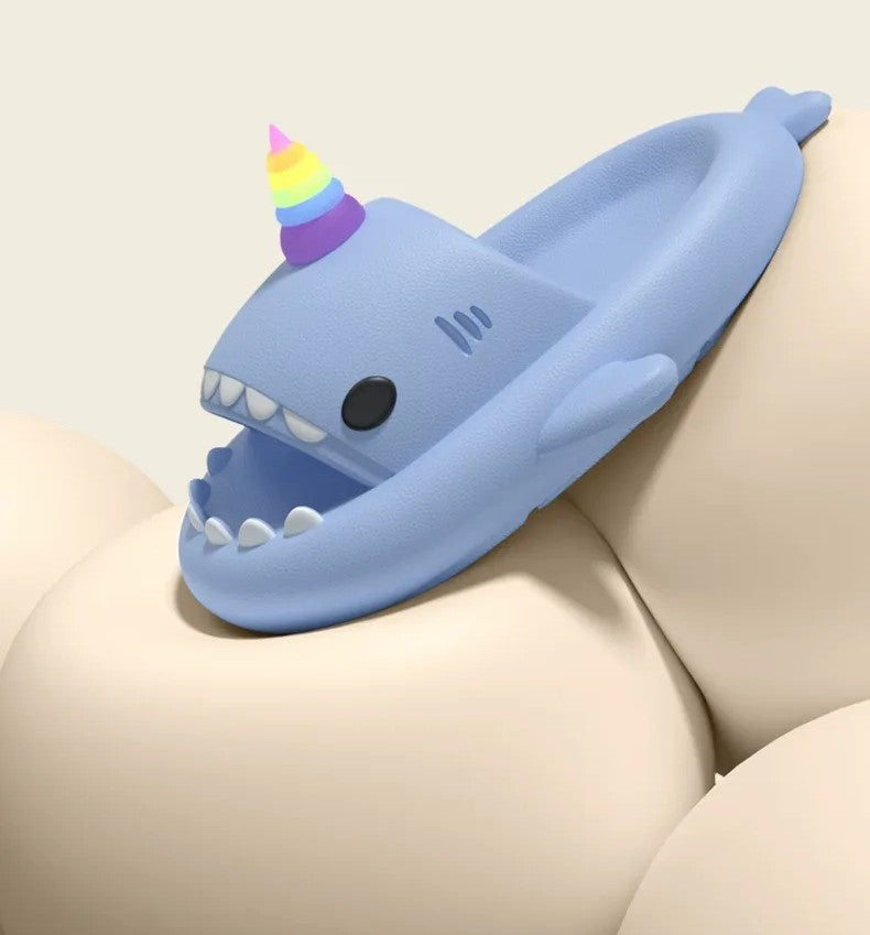 Blue shark-shaped slipper with a rainbow unicorn horn on a beige surface