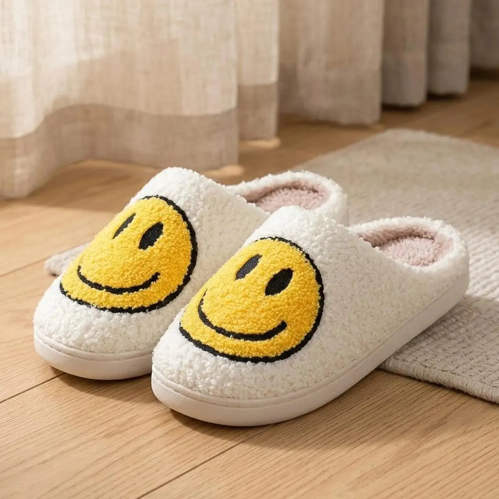 Pair of white slippers with yellow smiley face designs on a wooden floor.