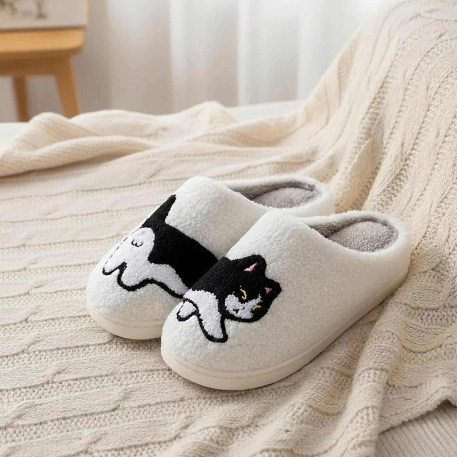 Pair of white slippers with a cat design on a textured surface