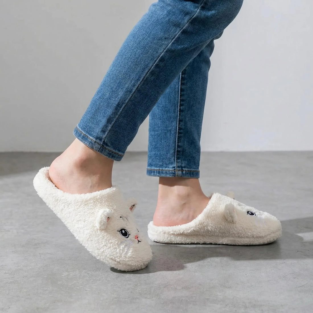 Black cat-shaped slippers worn on a beige carpet