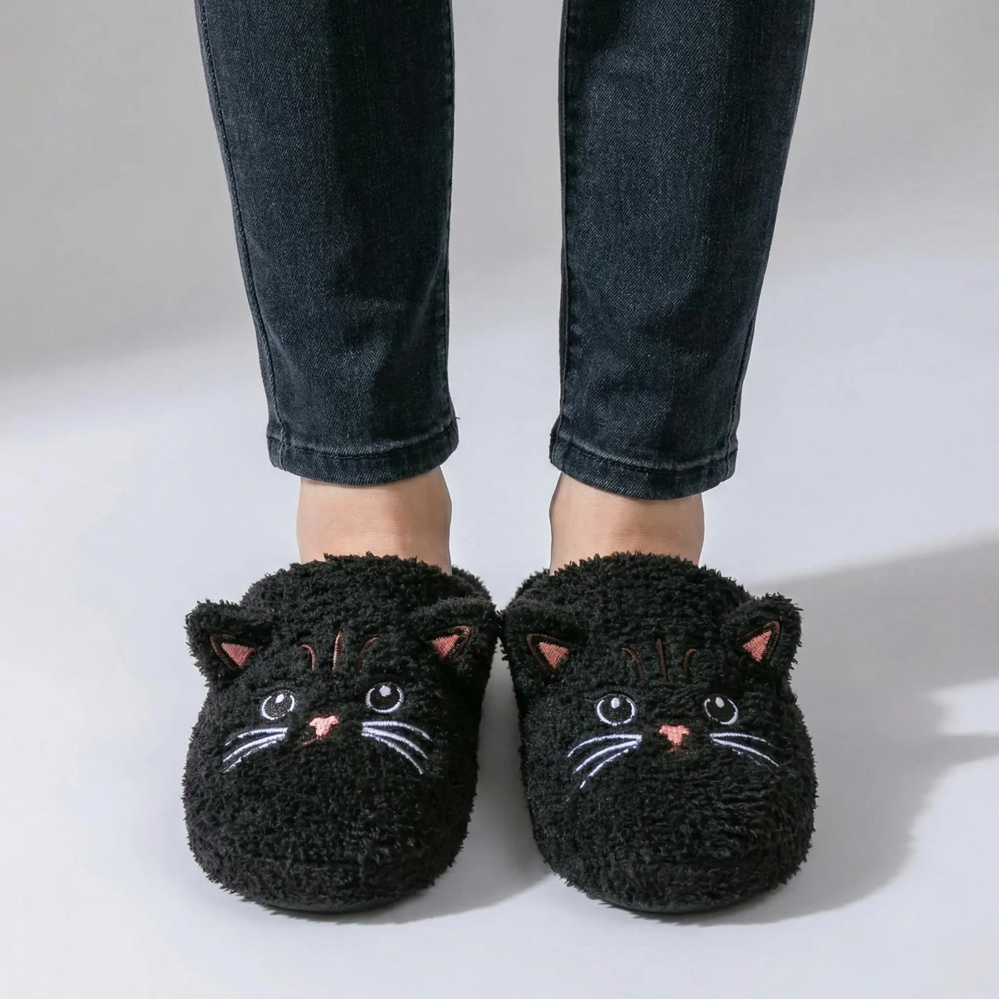 Black cat-shaped slippers worn with dark jeans on a light background
