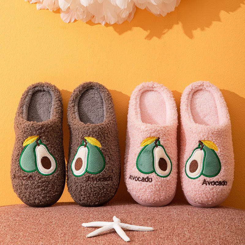 Pair of dark blue slippers with avocado design held against a yellow background