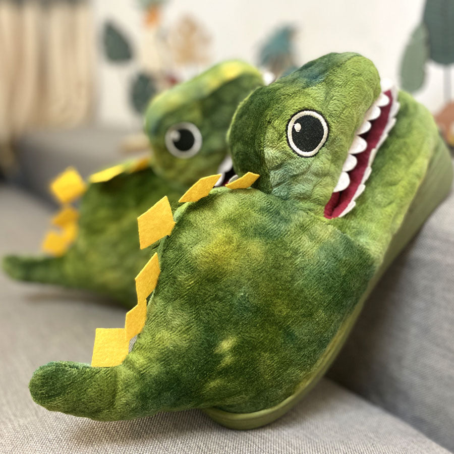 Green dinosaur-shaped slippers on a gray surface with a blurred background