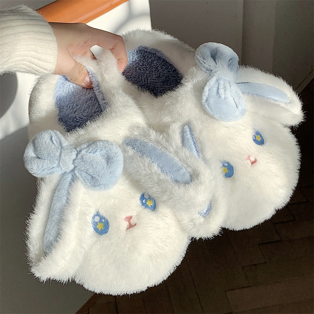 Pair of white bunny fuzzy slippers with blue accents held by a hand