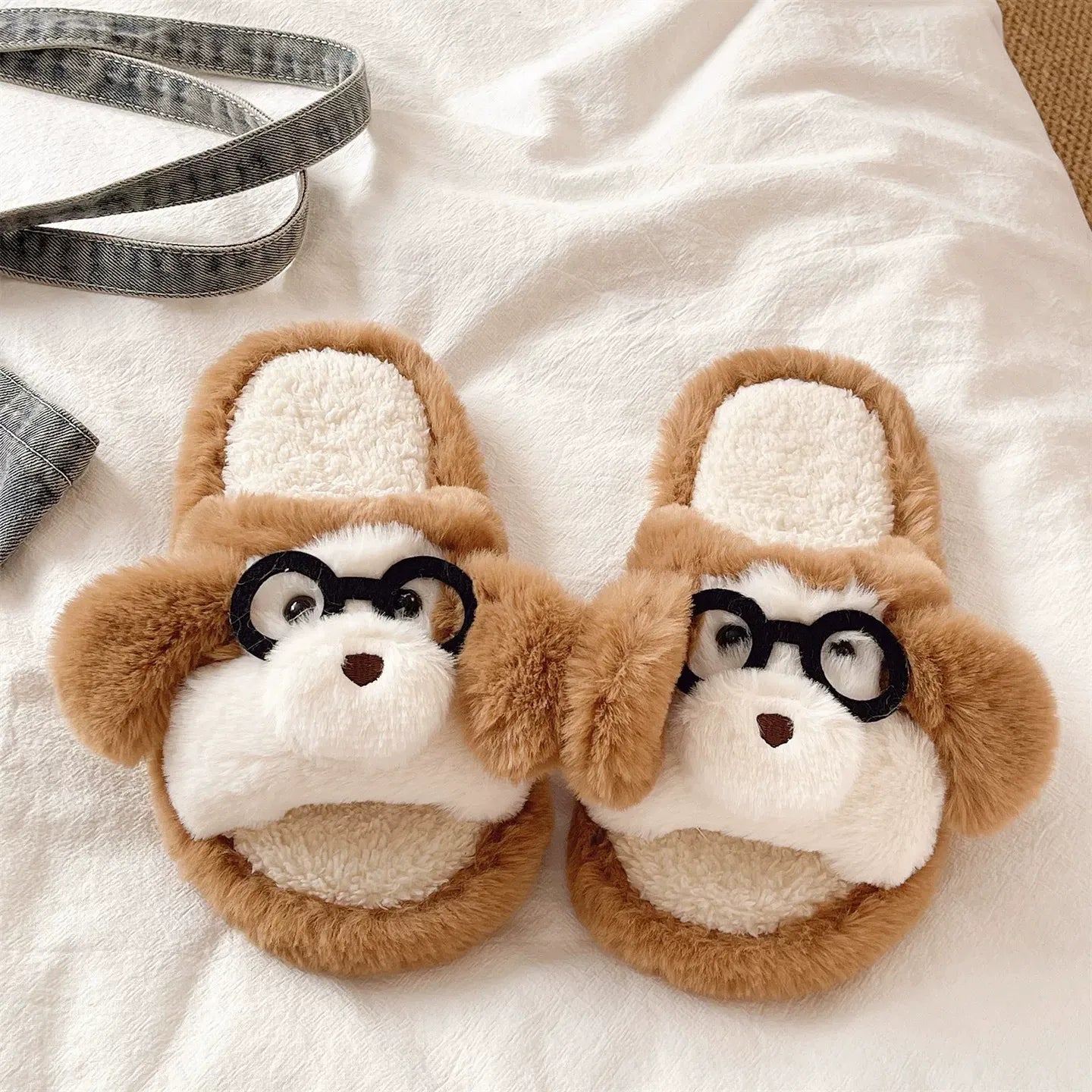 Pair of plush dog slippers with glasses on a soft white surface