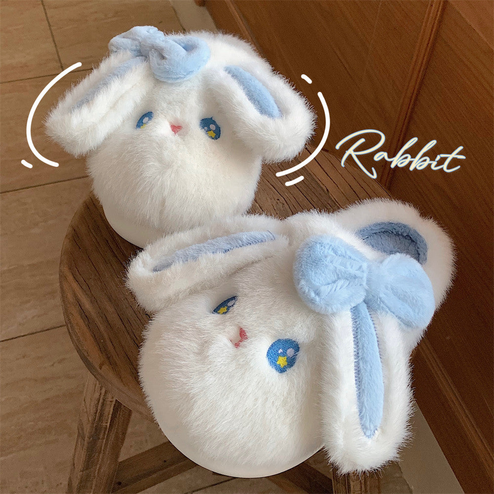 Two white plush rabbit slippers with blue bows on a wooden stool.
