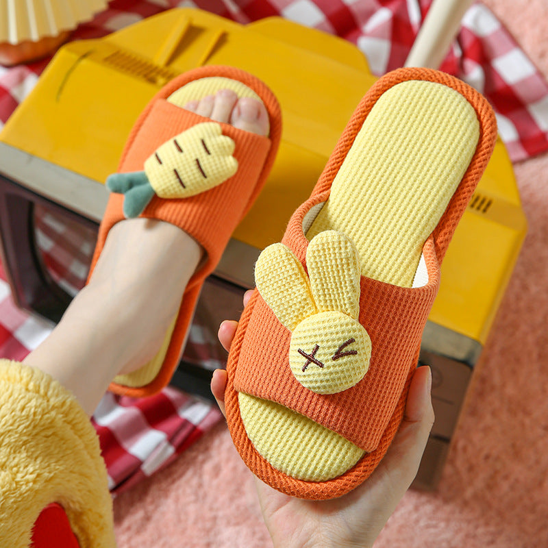 Pair of orange and yellow slippers with bunny designs held by a person.